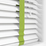 Close up of white wooden blinds with green tape